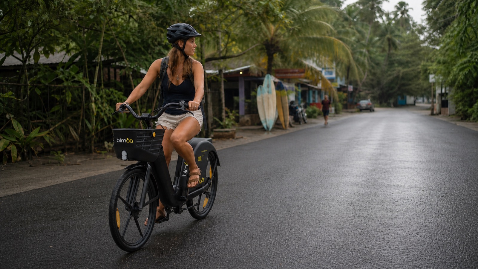 Helmeted rider using the exact black Bimba shared e-bike model on a wet asphalt road in Santa Teresa