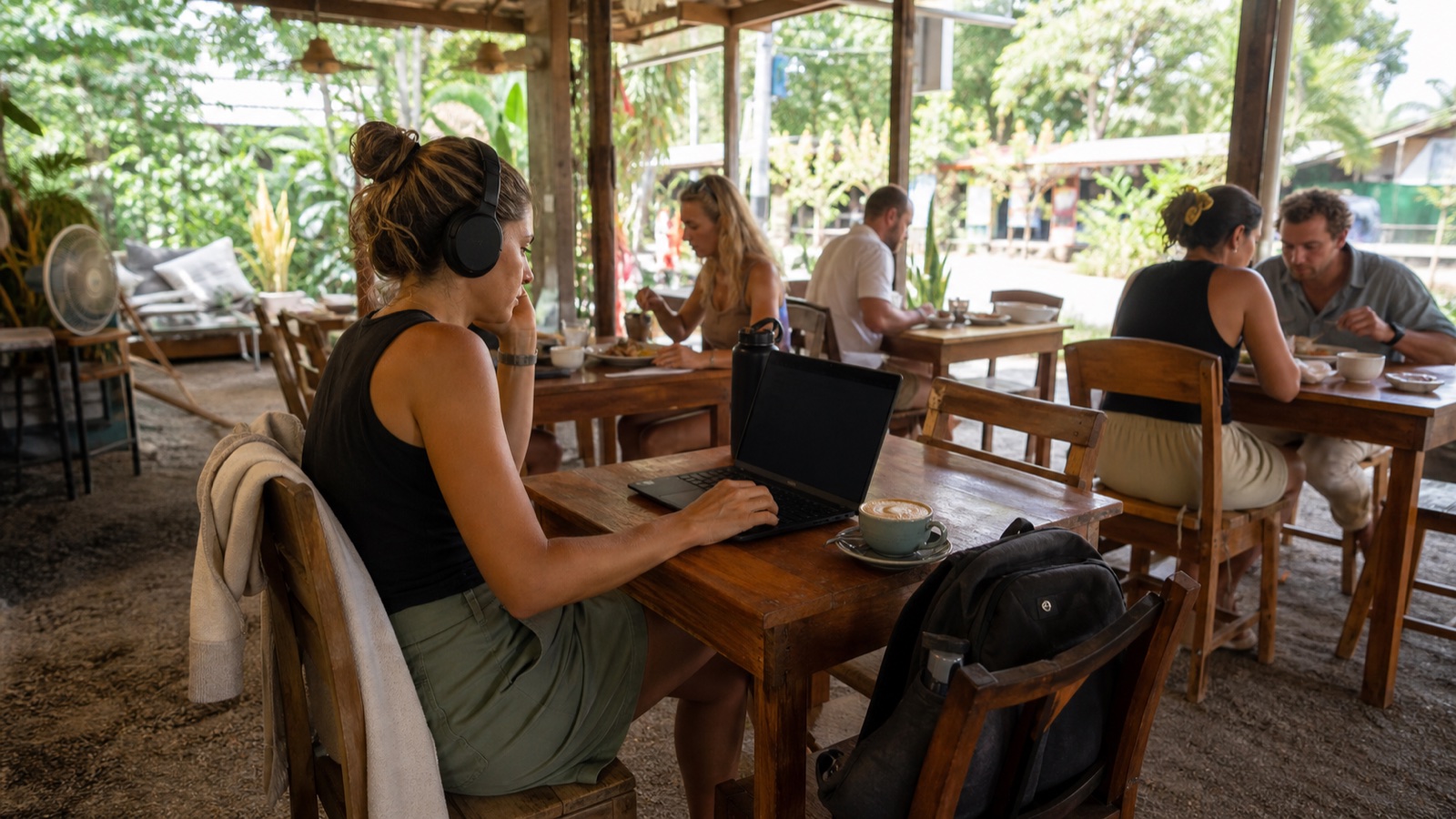 Traveler working quietly with headphones, a laptop and an ordered coffee at an open-air tropical café